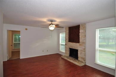 Unfurnished living room with healthy amount of natural light, dark wood-type flooring, a textured ceiling, ceiling fan, and a fireplace