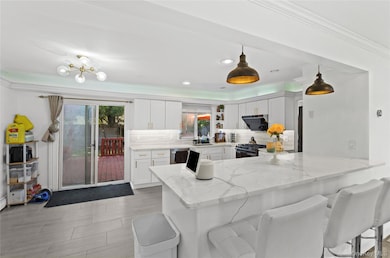 Kitchen with backsplash, light stone countertops, a peninsula, white cabinets, and crown molding