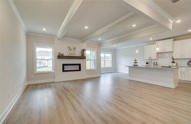 Unfurnished living room with ornamental molding, beam ceiling, light wood-style flooring, baseboards, and a glass covered fireplace