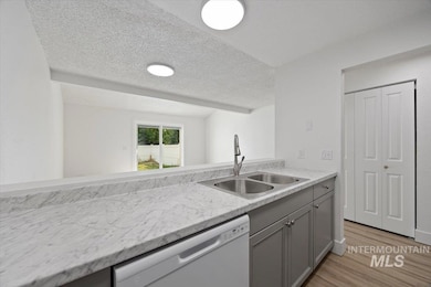 Kitchen with gray cabinets, a textured ceiling, white dishwasher, and light wood-style flooring