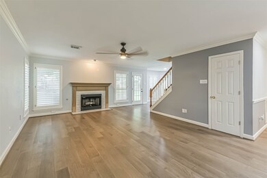 Spacious living area features hardwood floors, a cozy fireplace, and ample natural light from multiple windows. The room is complemented by a ceiling fan and has direct access to a staircase, offering a modern and inviting atmosphere.