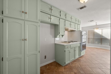 Kitchen featuring green cabinets, light countertops, light tile patterned floors, decorative light fixtures, and under cabinet range hood