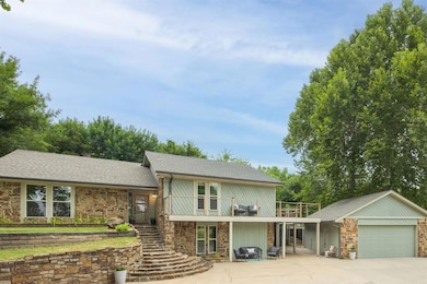 View of front of property featuring stone siding, stairs, roof with shingles, and a patio