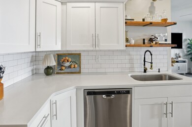 Kitchen with stainless steel dishwasher, white cabinetry, open shelves, and backsplash