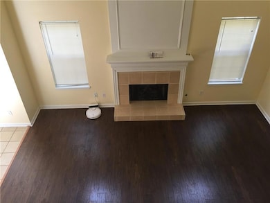 Unfurnished living room featuring dark wood finished floors, baseboards, and a tiled fireplace