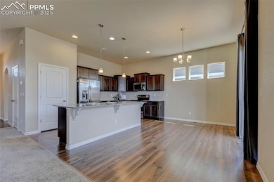 Kitchen with appliances with stainless steel finishes, wood finished floors, a chandelier, and dark brown cabinets