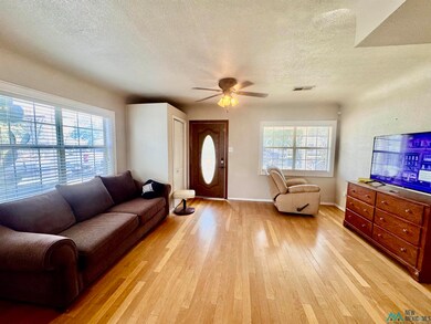 Living room with a textured ceiling, light wood-style flooring, and ceiling fan