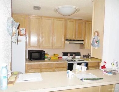 Kitchen with white appliances, light brown cabinetry, under cabinet range hood, light countertops, and a peninsula