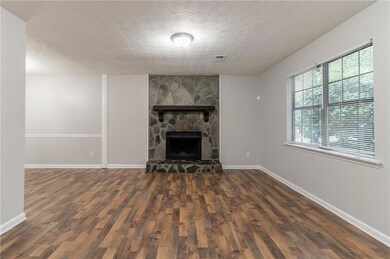 Unfurnished living room featuring wood finished floors, a textured ceiling, a stone fireplace, and baseboards