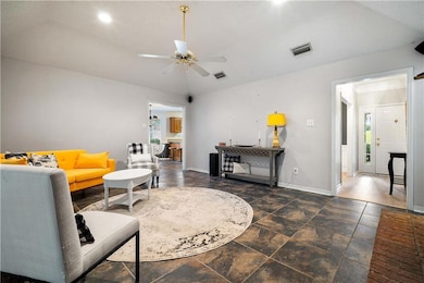Living area with healthy amount of natural light, dark stone finish floors, ceiling fan, and vaulted ceiling