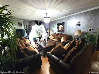 Living area featuring wood finished floors, wallpapered walls, crown molding, and a chandelier