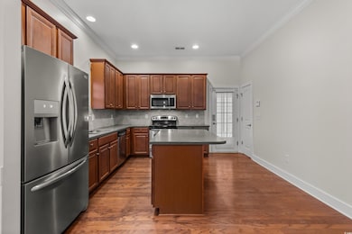 Kitchen with dark countertops, stainless steel appliances, tasteful backsplash, dark wood-type flooring, and crown molding