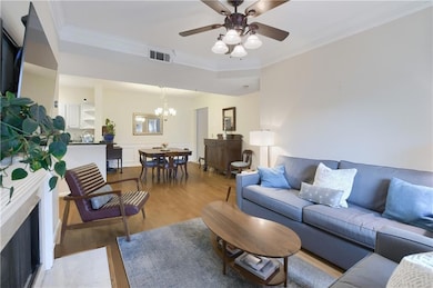 Living room with crown molding, light wood-type flooring, a chandelier, a ceiling fan