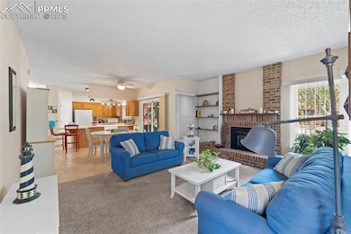 Living area with a textured ceiling, a fireplace, a ceiling fan, light colored carpet, and light tile patterned floors
