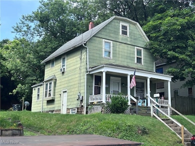View of front of house featuring covered porch, a chimney, view of scattered trees, and a front yard