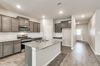 Kitchen featuring decorative backsplash, stainless steel appliances, light stone counters, light wood-type flooring, and a center island with sink