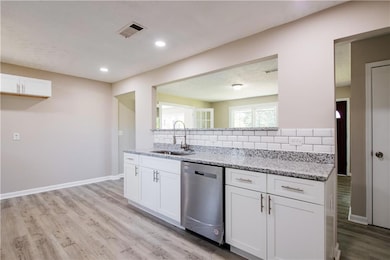 Kitchen featuring a sink, white cabinetry, stainless steel dishwasher, visible vents, and decorative backsplash