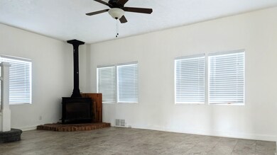 Unfurnished living room featuring a wood stove and a ceiling fan