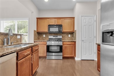 Kitchen with stainless steel appliances, light stone countertops, backsplash, light wood finished floors, and brown cabinetry