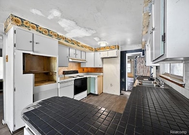 Kitchen featuring tile counters, white appliances, a peninsula, white cabinetry, and under cabinet range hood