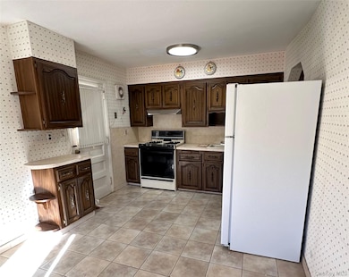 Kitchen with wallpapered walls, freestanding refrigerator, light countertops, range with gas stovetop, and light tile patterned floors
