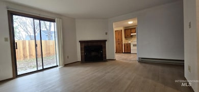 Unfurnished living room with a brick fireplace, light wood-style flooring, and a baseboard heating unit