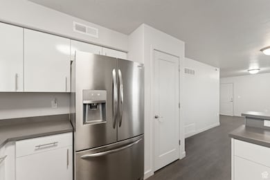 Kitchen featuring dark countertops, stainless steel fridge with ice dispenser, dark wood-style flooring, white cabinets, and a textured ceiling