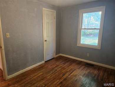Unfurnished room featuring a textured wall and dark wood-type flooring