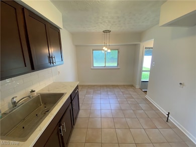 Kitchen with decorative light fixtures, light tile patterned floors, light stone counters, a textured ceiling, and decorative backsplash