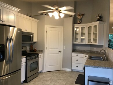 Kitchen with dark countertops, glass insert cabinets, stainless steel appliances, white cabinetry, and a sink