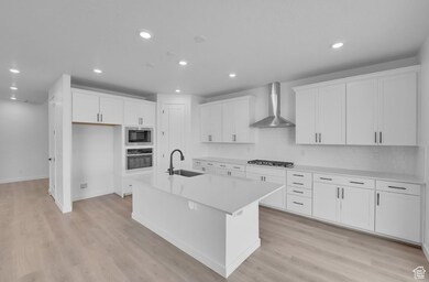 Kitchen with white cabinets, wall chimney exhaust hood, recessed lighting, an island with sink, and light wood-style floors