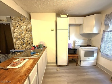 Kitchen featuring white range with electric stovetop, white cabinetry, a textured ceiling, light wood-type flooring, and black microwave
