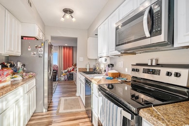 Kitchen featuring appliances with stainless steel finishes, white cabinets, light wood-type flooring, and a textured ceiling