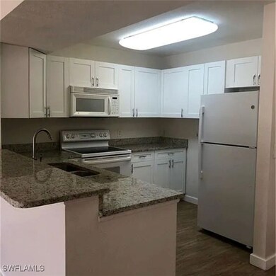 Kitchen with a peninsula, white appliances, white cabinets, and stone counters