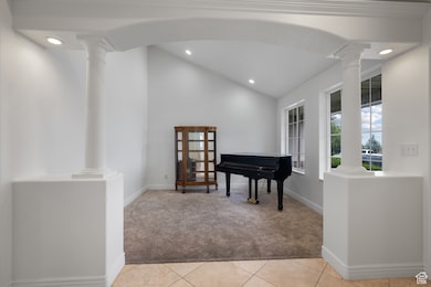 Living area featuring light colored carpet, decorative columns, vaulted ceiling, light tile patterned floors, and recessed lighting