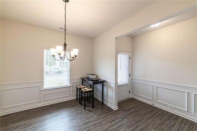 Dining room featuring a chandelier, a wainscoted wall, healthy amount of natural light, dark wood-style floors, and a decorative wall