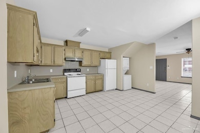 Kitchen featuring white appliances, light tile patterned floors, stacked washer and clothes dryer, ceiling fan, and sink