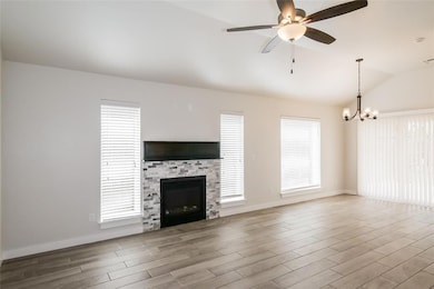 Unfurnished living room with vaulted ceiling, wood finished floors, a glass covered fireplace, ceiling fan, and a chandelier
