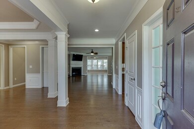 Foyer featuring a fireplace, dark wood finished floors, a ceiling fan, crown molding, and ornate columns