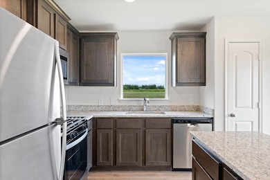 Kitchen with stainless steel appliances, dark brown cabinets, light wood finished floors, light stone counters, and recessed lighting