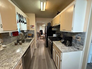 Kitchen with black gas range, stainless steel dishwasher, wood finished floors, under cabinet range hood, and decorative backsplash
