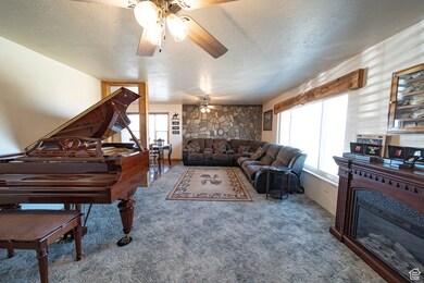 Carpeted living area with a textured ceiling, a fireplace, and a ceiling fan
