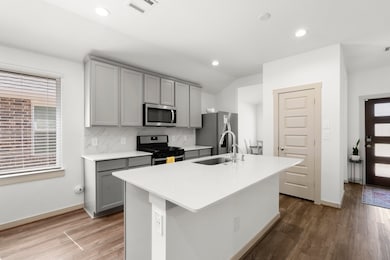 The kitchen features stylish grey cabinets, sleek stainless steel appliances, a spacious pantry for extra storage, and a large kitchen island perfect for meal prep and gathering.