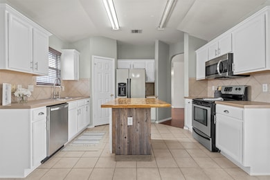 Kitchen featuring appliances with stainless steel finishes, light tile patterned floors, light countertops, tasteful backsplash, and white cabinetry