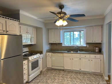 Kitchen with white appliances, crown molding, white cabinetry, ceiling fan, and dark stone counters