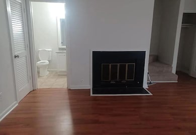 Unfurnished bedroom with a glass covered fireplace, dark wood-type flooring, a closet, and connected bathroom