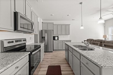 Kitchen with appliances with stainless steel finishes, gray cabinetry, light wood-style floors, and a center island with sink
