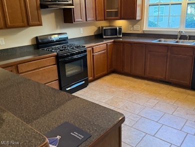 Kitchen featuring dark countertops, black gas range, brown cabinets, stainless steel microwave, and under cabinet range hood