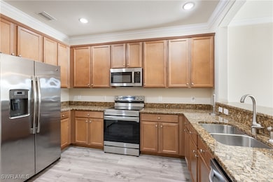 Kitchen with stainless steel appliances, crown molding, dark stone countertops, brown cabinets, and light wood finished floors