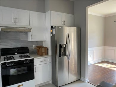 Kitchen featuring stainless steel fridge, range with gas cooktop, under cabinet range hood, crown molding, and white cabinetry